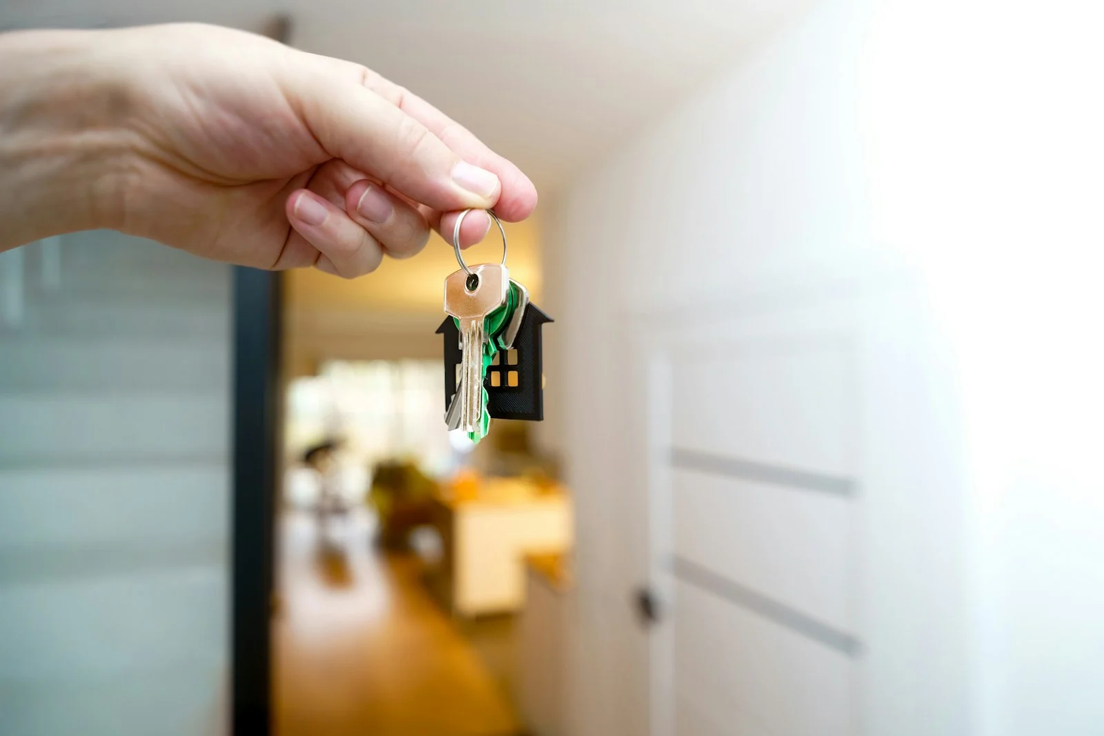 immobilier-cles-maison Main qui tient un trousseau de clés devant l’entrée d’une maison
